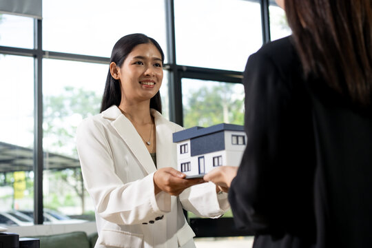 Woman presenting a small house model to a client in a bright office during a real estate meeting