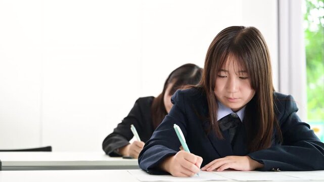 綺麗な新緑背景の教室で真剣にテストや模試へ取り組む日本人女子中学生や高校生複数　受験や定期テスト受ける動画