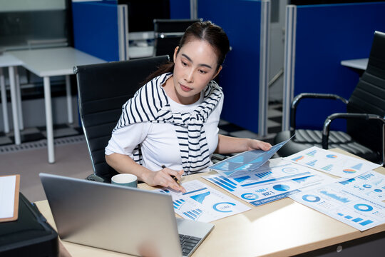 Businesswoman reviewing financial charts and reports at a desk with laptop in a modern office