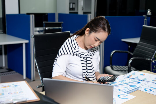 Young businesswoman using calculator and reviewing financial charts at office desk