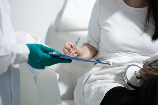 Doctor holding a clipboard while a patient signs a medical form during a consultation in a bright clinic