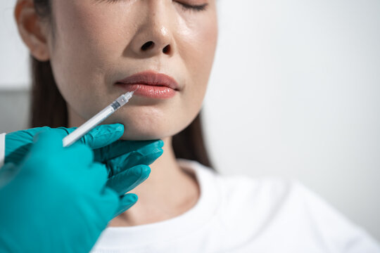 Close-up of a woman receiving a cosmetic lip injection from a gloved medical professional in a clean clinic setting