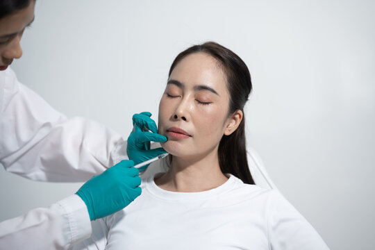 Doctor giving lip filler injection to a woman in a clean clinic, with patient sitting calmly during cosmetic treatment