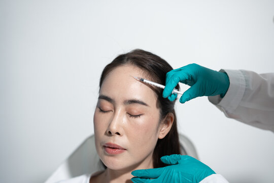 A woman receiving a cosmetic forehead injection from a gloved doctor in a clean clinic, with eyes closed during a beauty treatment.
