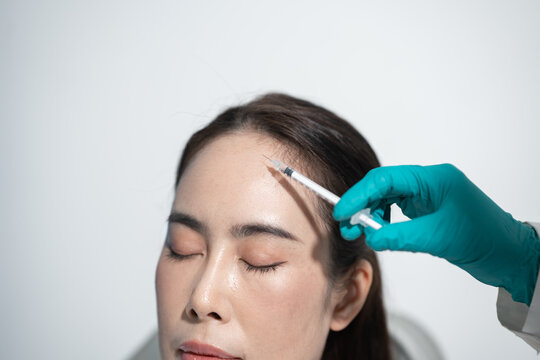 A woman receives a facial injection on the forehead from a gloved doctor in a clean clinic, showing cosmetic treatment and skin care.