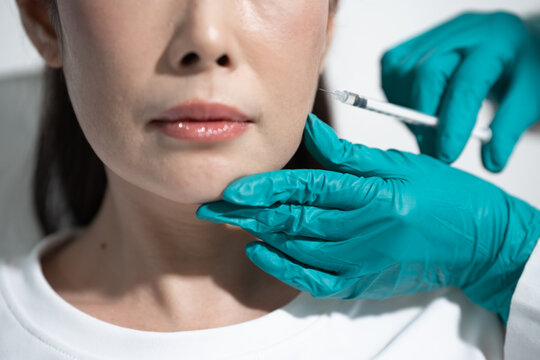 Close-up of a woman receiving a cosmetic facial injection with gloved hands in a clinic setting.