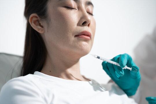 Close-up of a woman receiving a cosmetic injection in the neck from a gloved medical professional in a clean clinic.