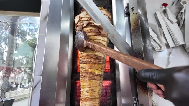 Chef carving succulent doner kebab meat with sharp knife from vertical rotisserie, cinematic street food preparation footage
