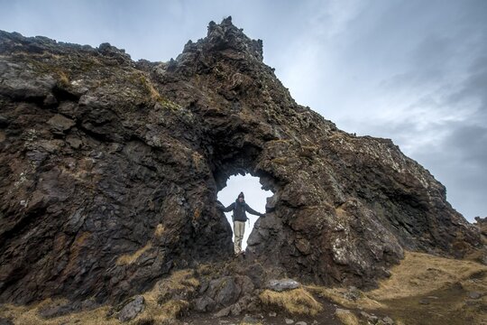 Young man stands in rock arch, volcanic rock on the beach of Dj&uacute;pal&oacute;nssandur, Sn&aelig;fellsnes peninsula, West Iceland, Iceland