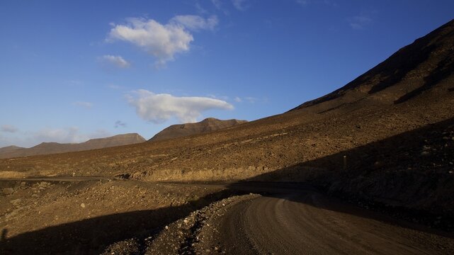 Wild South, Jandia, barren landscape, non-asphalted road, reddish brown hills, blue sky, few clouds, Fuerteventura, Canary Islands, Spain
