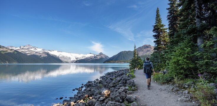 Hikers on the shore of Garibaldi Lake, mountains reflected in the turquoise glacial lake, Guard Mountain and Deception Peak, glacier in the back, Garibaldi Provincial Park, British Columbia, Canada