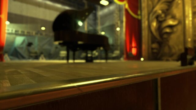 Dimly lit theater stage with piano, low angle view from edge of proscenium, red velvet curtain and gilded ornament, warm spotlight creating soft haze and dust
