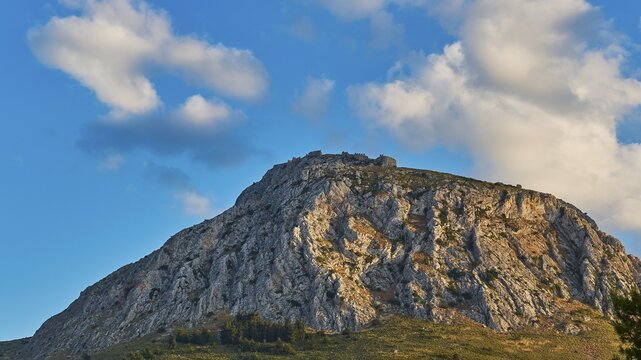 The sun shines on a rocky mountain under a cloudy blue sky, Archaic Castle, Akrokorinthos, Corinth, Peloponnese, Greece