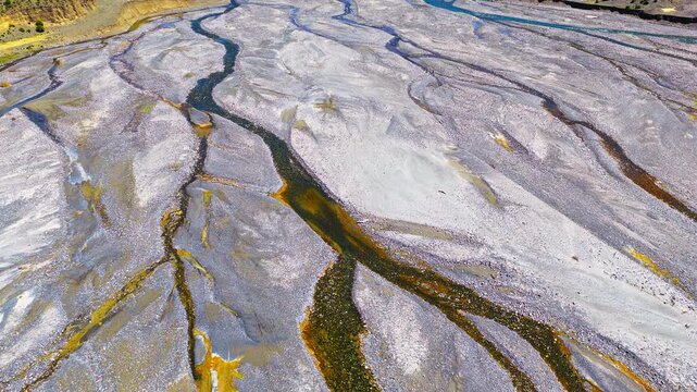Aerial view of a braided river system with winding water channels carving through a rocky gray gravel bed in Xinjiang, China.