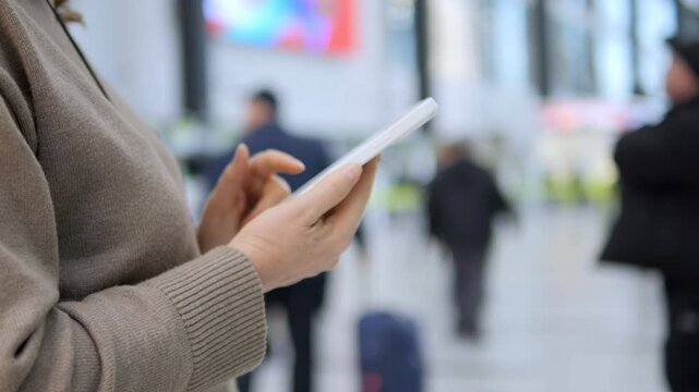 Person holds tablet in busy public space. Hands focus on device while background moves. Crowds pass by, creating sense of travel or transit. Suitable for themes like technology, commuting