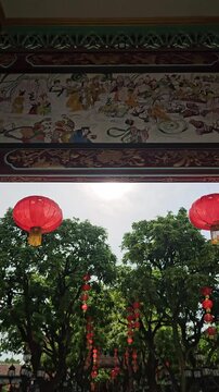 Vertical tilt down shot from a painted heritage ceiling to red lanterns and a young woman standing on a scenic path in Baomo Garden, Guangzhou.