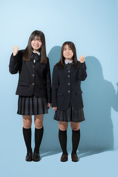 水色背景で未来や将来へ向かってがんばるガッツポーズカメラ目線全身　日本人女子高生や中学生の全身　2人で前向きに進む受験や青春、合格やオープンキャンパスイメージ