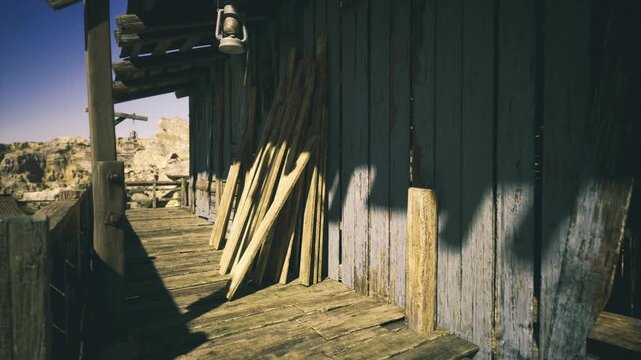 Sunlit western porch with stacked planks, warm golden light casting long shadows across weathered blue siding and dusty boardwalk, rough timber grain and rusty