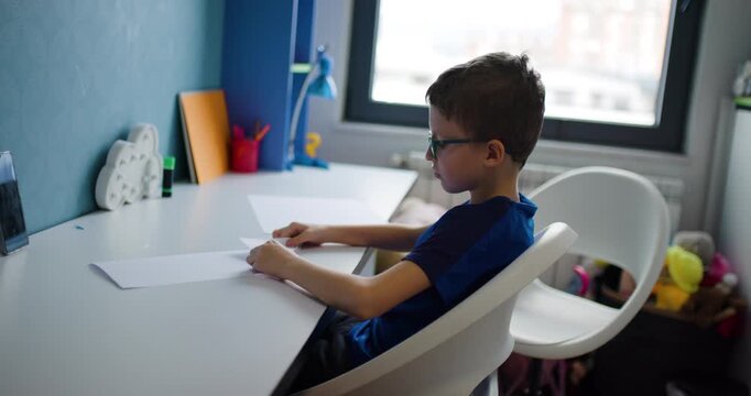 Young Boy with Glasses Folds Paper at Desk in Colorful Bedroom, Engaged in Creative Activity