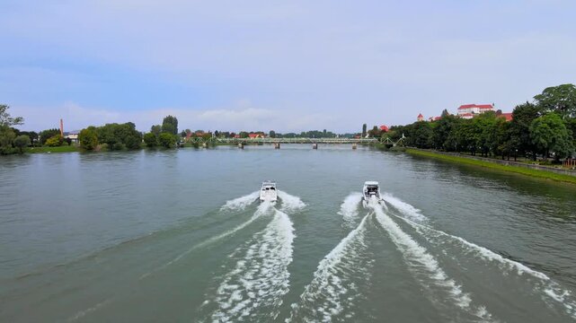 Aerial footage captures boats gliding over the Drava river in Ptuj, Slovenia, showcasing vibrant waters, green banks, historic city, and dynamic motion.