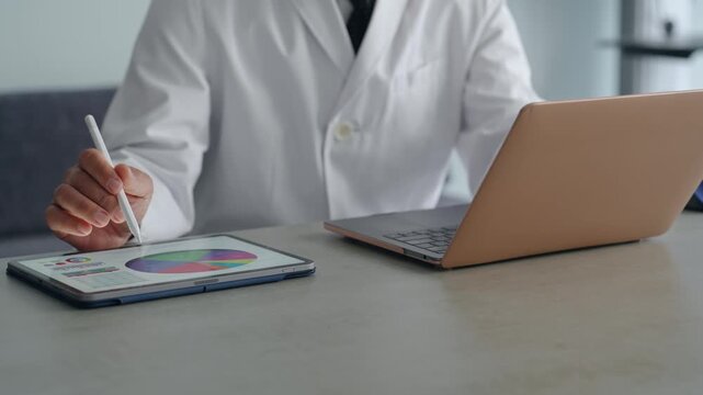 ノートパソコンとタブレットPCを使って作業する白衣の男性。医療、科学、研究、開発、経営、DX、AI