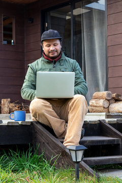 Digital nomad working on a laptop while sitting on the steps of a wooden cabin