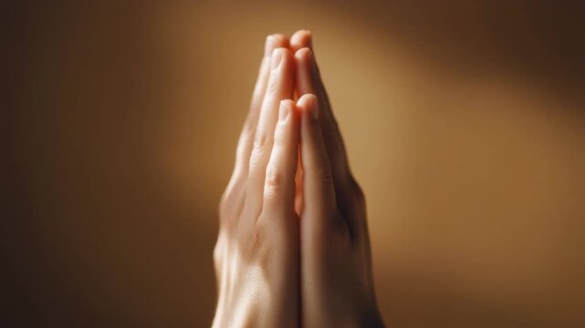Close-up of hands pressed together in prayer gesture with warm golden light expressing gratitude and faith