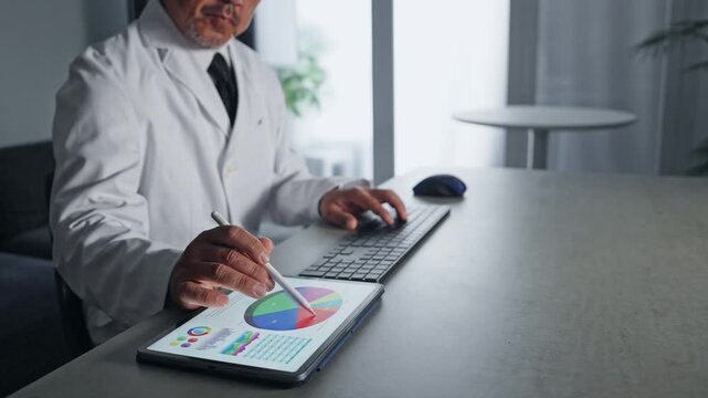 パソコンとタブレットPCを使って作業する白衣の男性。科学、研究、DX、IT、医療、医師、開発、データ