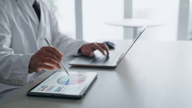 ノートパソコンとタブレットPCを使って作業する白衣の男性。科学、研究、医療、医師、実験、データ、分析