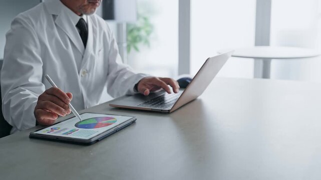 ノートパソコンとタブレットPCを使って作業する白衣の男性。科学、研究、医療、医師、実験、データ、分析