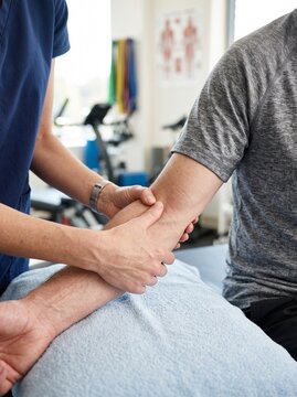 Physical therapist examining and massaging male patient arm in clinic