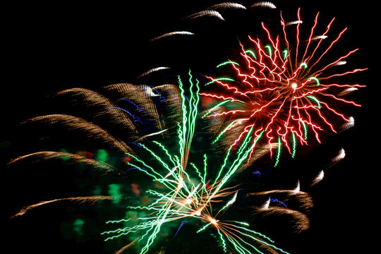 Colorful red and green fireworks exploding in the dark night sky during a celebration