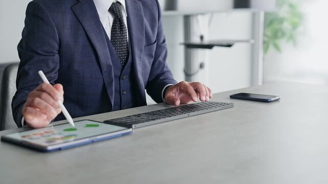 パソコンとタブレットPCを使って作業する男性。デスクワーク、ビジネス、仕事、業務、オフィス、制作