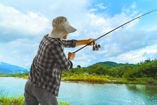 Back view of man fishing by river under blue sky