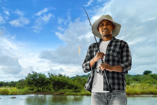 Portrait of man smilling with fishing rod by river under blue sky