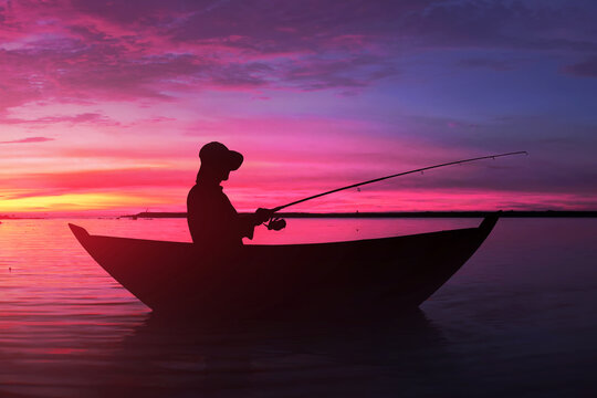 Silhouette of man fishing from wooden boat at sunset