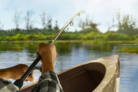 Man fishing from wooden boat on calm lake under blue sky