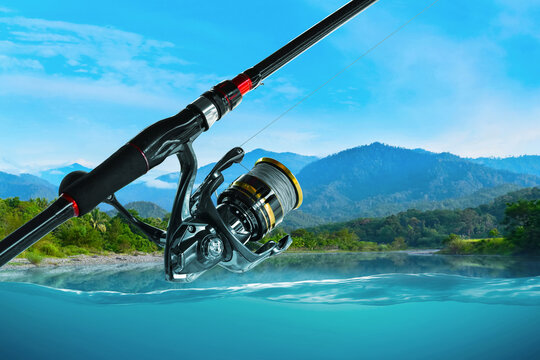 Closeup of fishing rod and spinning reel over calm lake and mountain landscape view