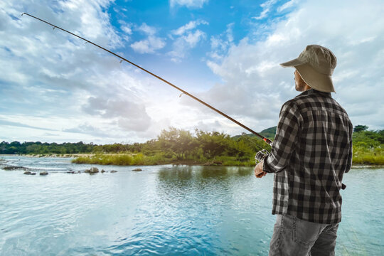 Back view of man fishing by river under blue sky
