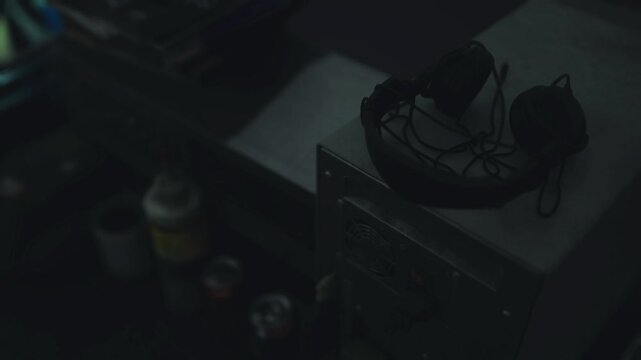 Black studio headphones resting on equipment case near jars and cables, silent studio or workshop vibe, worn earcups and textured headband visible, ambient