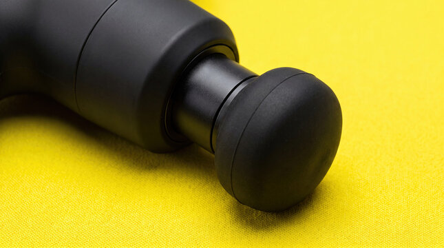 Black handheld massage gun on yellow surface closeup