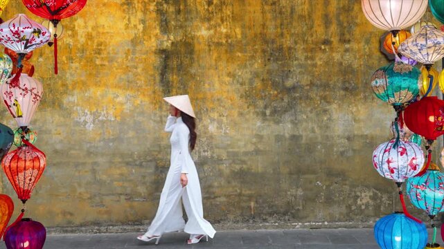 Asian woman wearing traditional Vietnamese culture walks beside an old wall in Hoi An, Vietnam.