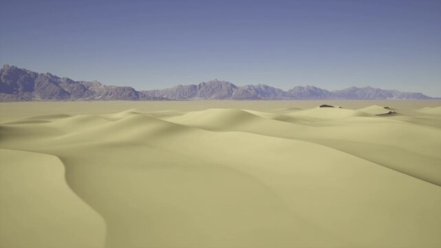 Vast golden sand dunes rise and fall gently beneath a clear blue sky. Majestic mountains stand in the distance, creating a stunning contrast against the endless expanse of sand.