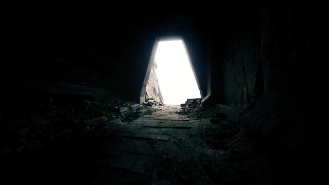 Bright rectangular opening ahead. Rough stone edges surround luminous opening. Shadowy cavern with debris leading to bright rectangular glow in distance