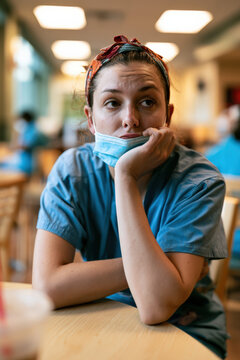 Young nurse rests chin on hand, mask tucked under head