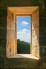 Obraz premium A landscape of blue sky, clouds and coastal bush framed in a window opening in Boyd's Tower, an intended but rejected lighthouse built of sandstone in Beowa National Park near Eden in Australia.