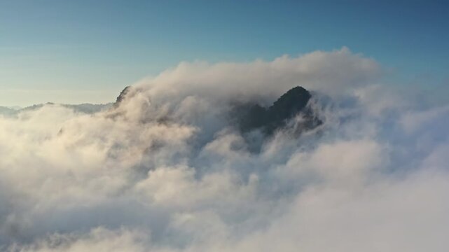 Limestone mountain karsts and peaks in Khao Sok National Park, Thailand, emerge from thick blanket of morning fog and clouds, catching the soft light of a rising sun. Aerial view drone flight panorama