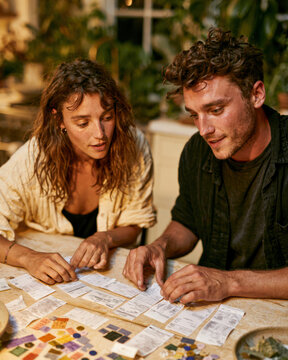 Two people sit at a table, focused on colorful tiles and notes