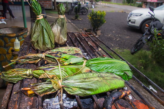 The traditional Amazonian dish maito in Ecuador: fresh river fish or local ingredients, tightly wrapped in green bijao or banana leaves, are roasted over hot charcoal grills at a roadside restaurant