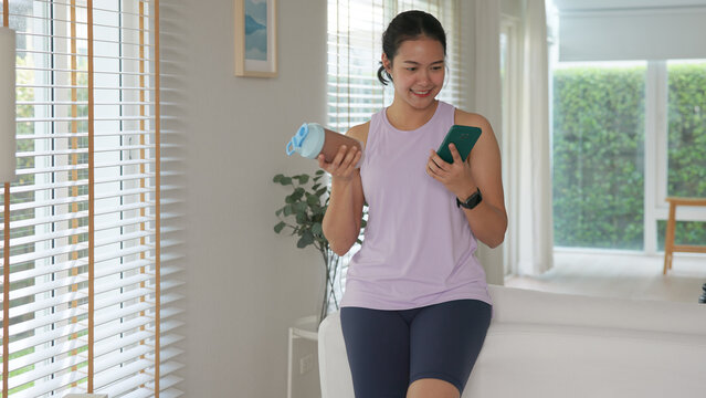 Young gen z active woman drink whey creatine shake bottle eating diet food using phone calorie plan app after home sport workout. health care asia people happy relax protect aging life weight loss.